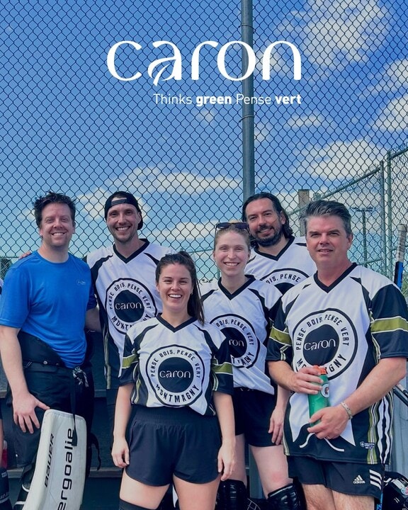 Équipe souriante devant un grillage avec logos Caron.
