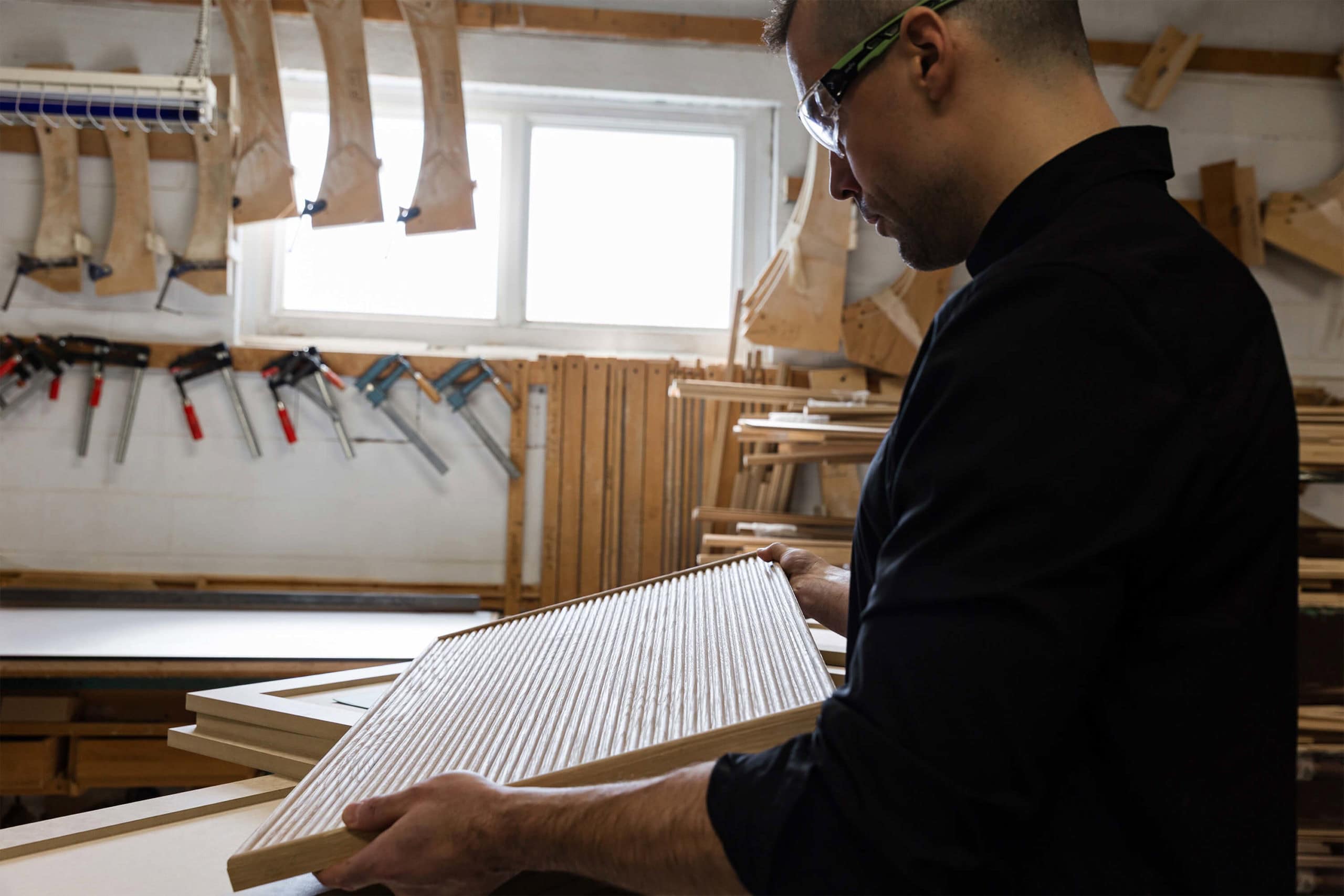 Woodworker in workshop holding wooden panel.