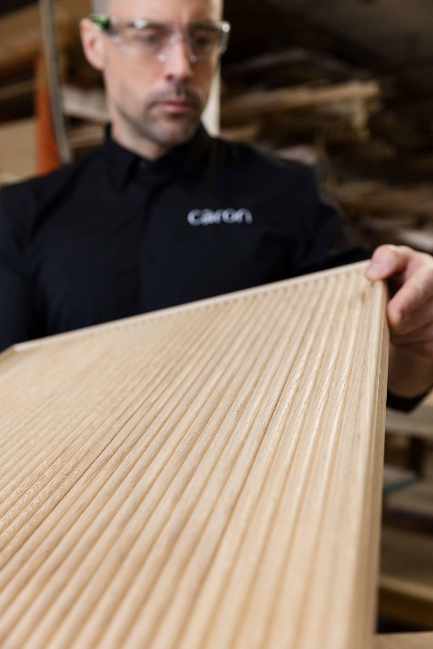 Person examining textured wooden panel in workshop.